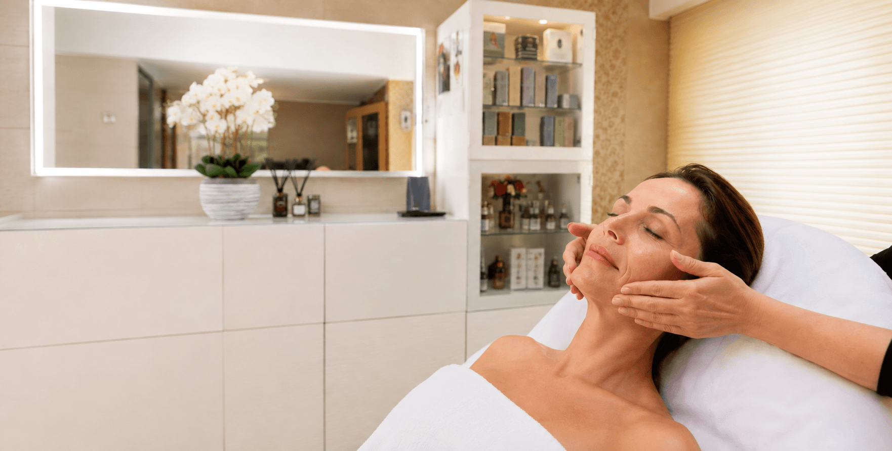Cliente détendue recevant un soin visage, geste doux des mains de la praticienne